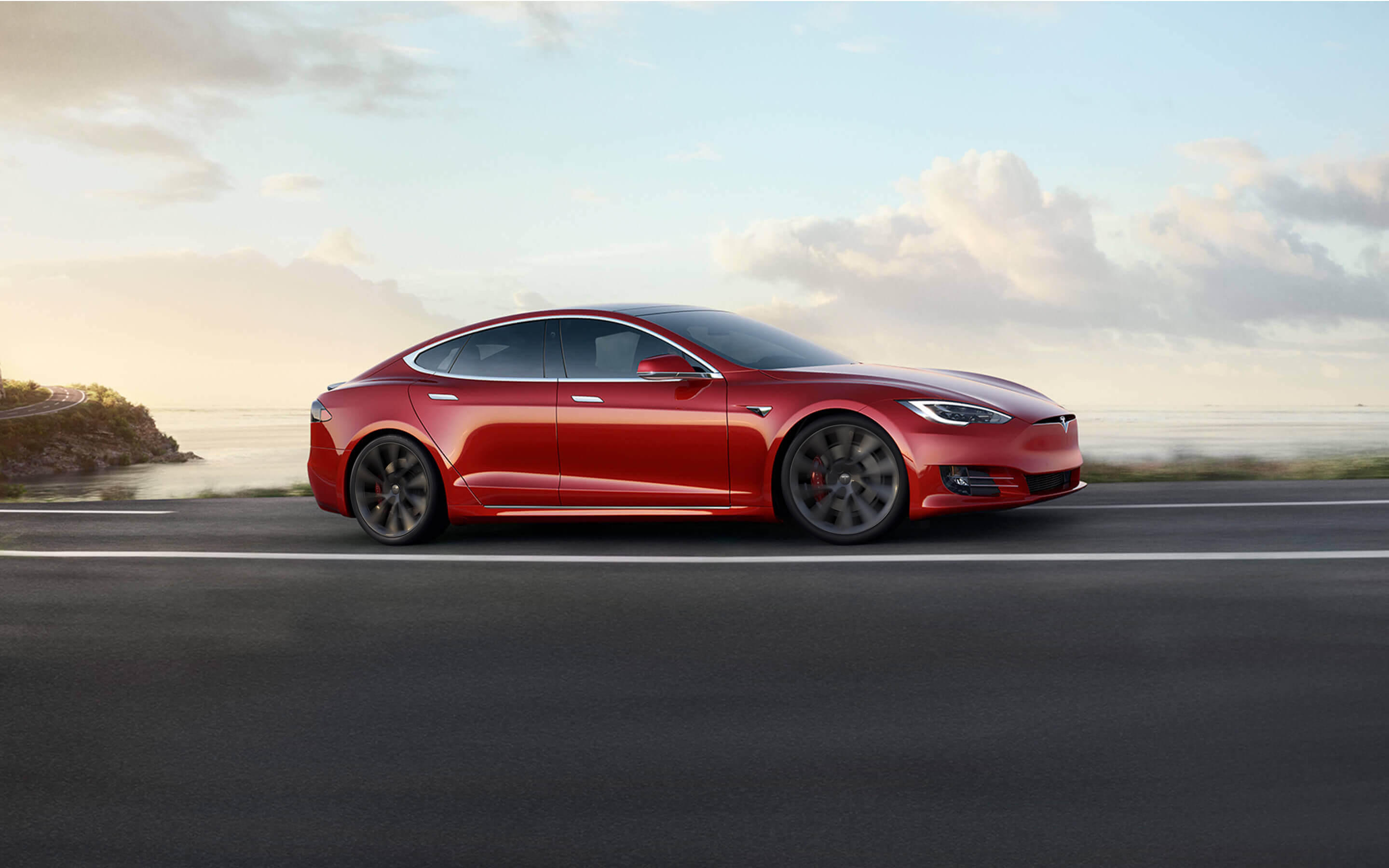 Red Model S accelerating down an oceanside highway